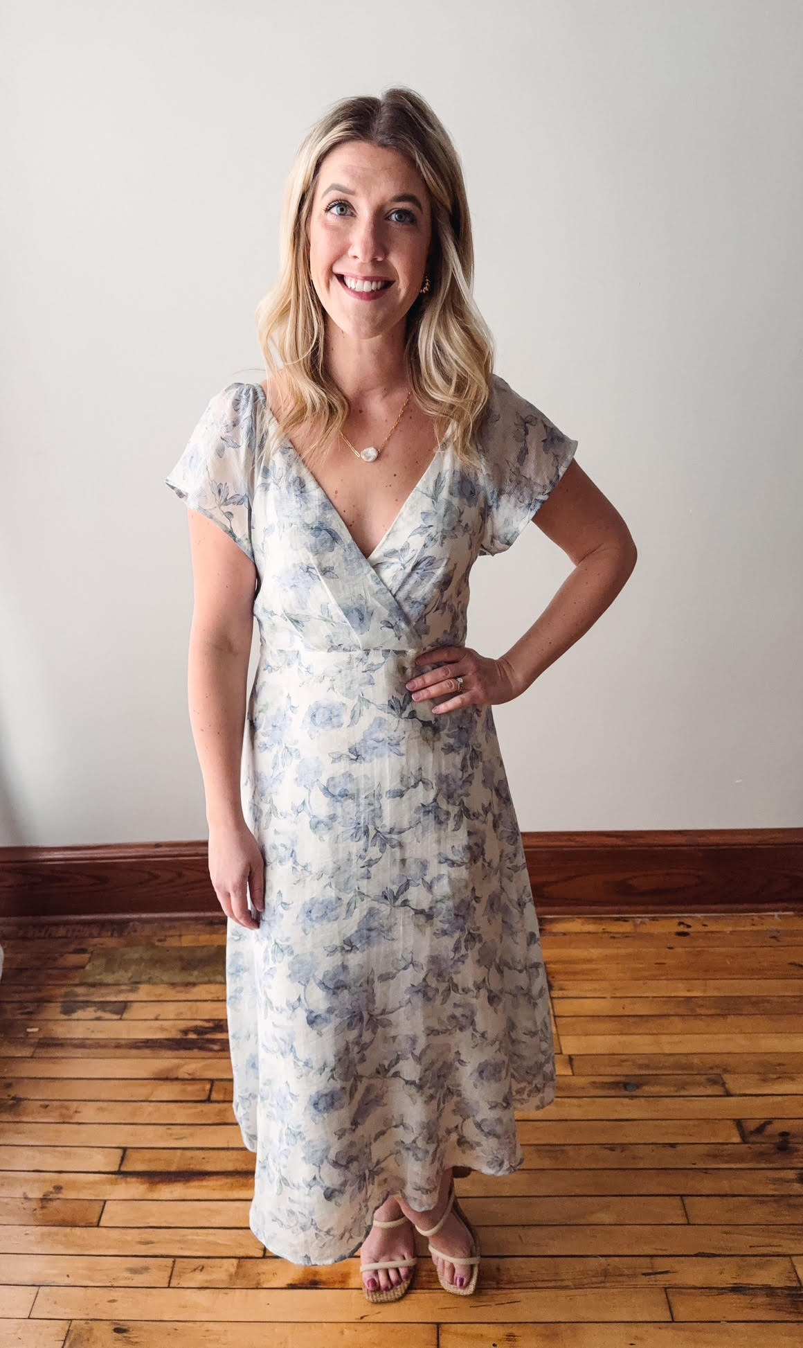 Woman wearing a floral dress standing on a wooden floor with a white wall background