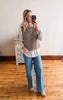 Woman taking a mirror selfie wearing a brown knitted vest over a white shirt and blue jeans.