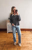 Woman taking a mirror selfie wearing a striped sweater and jeans in a room with wooden flooring.
