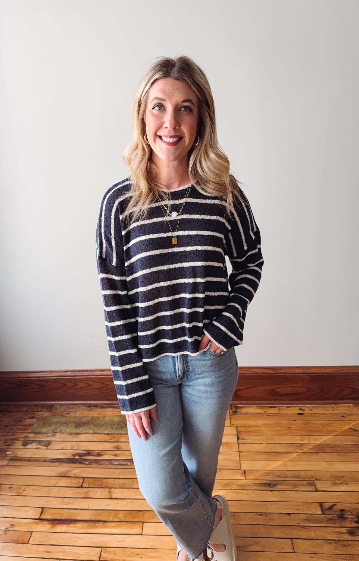 Woman wearing a striped sweater and jeans standing on a wooden floor.