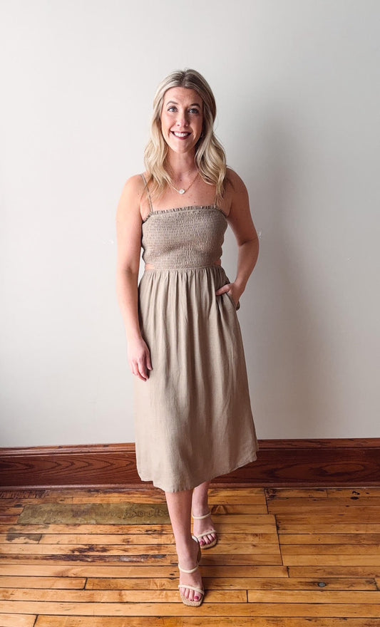 Woman wearing a beige strapless dress standing on a wooden floor with a white wall background