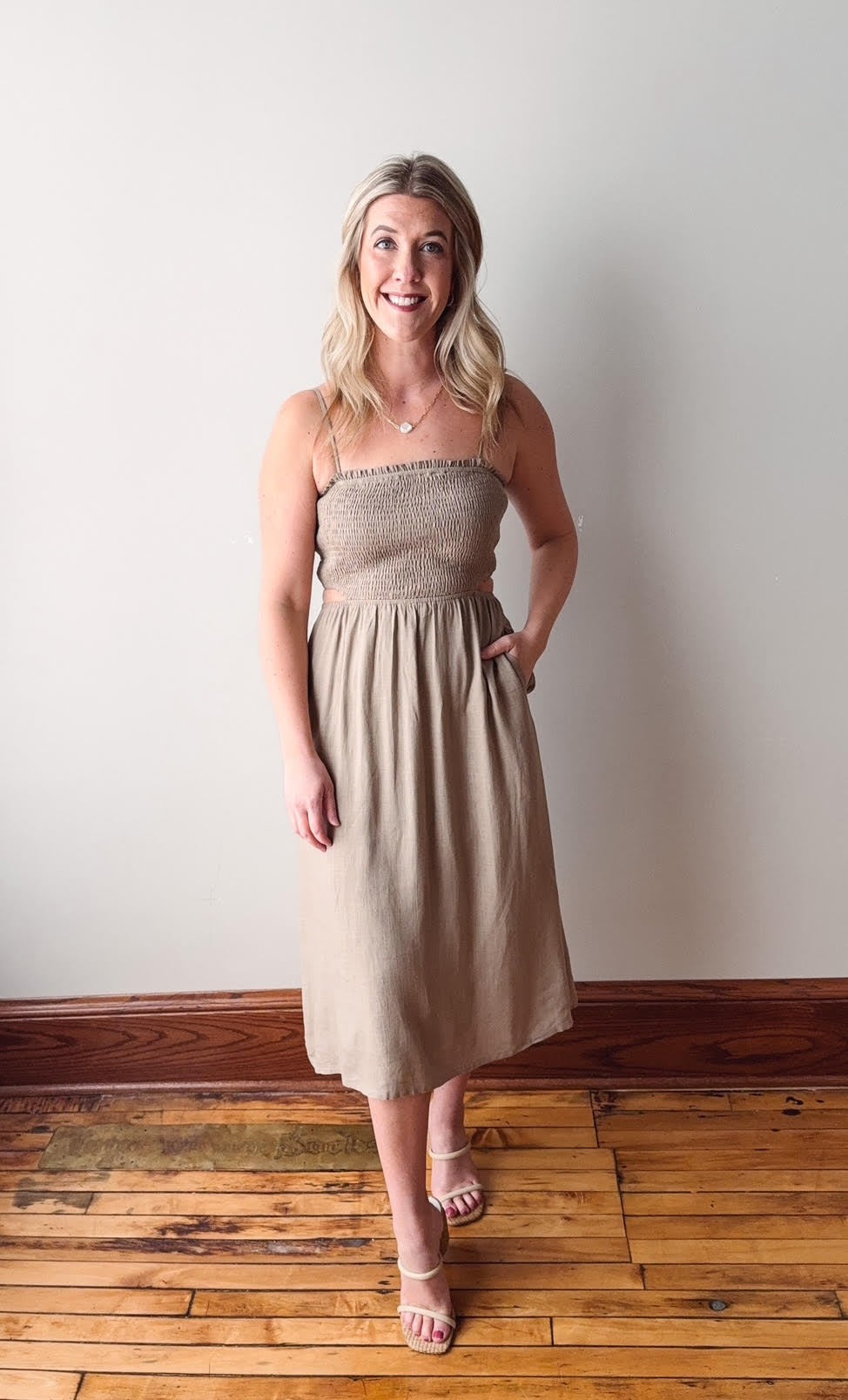 Woman wearing a beige strapless dress standing on a wooden floor with a white wall background