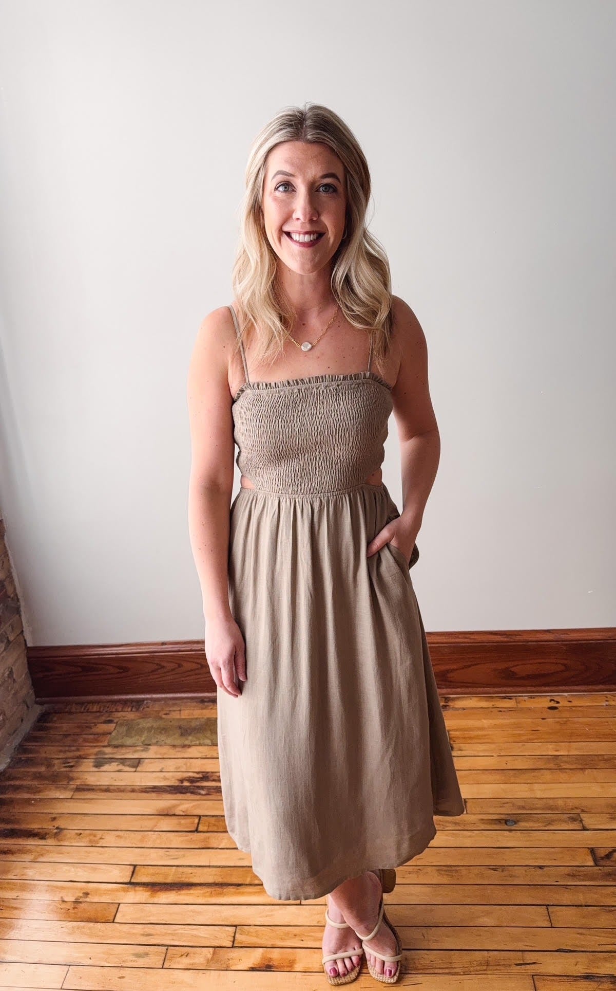 Woman wearing a beige dress standing on a wooden floor with a white wall background