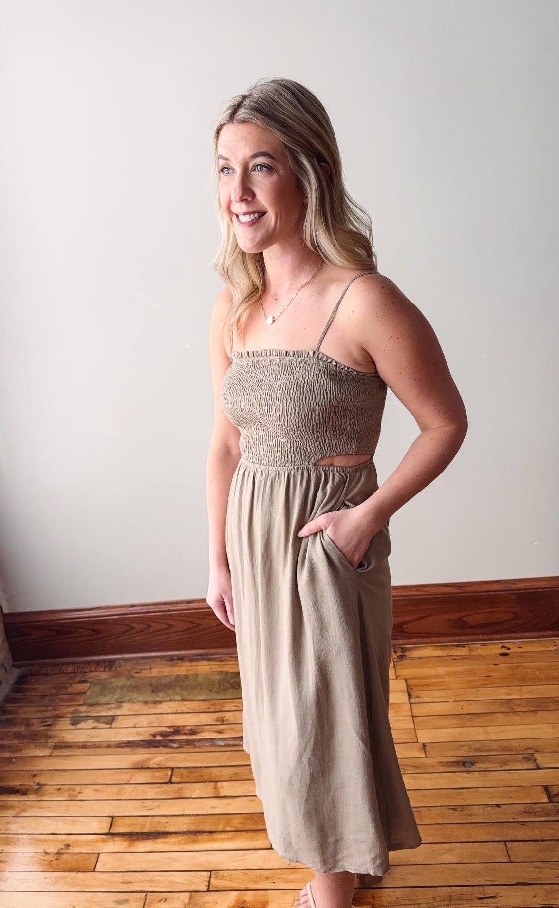 Woman wearing a beige dress standing on a wooden floor with a white wall background