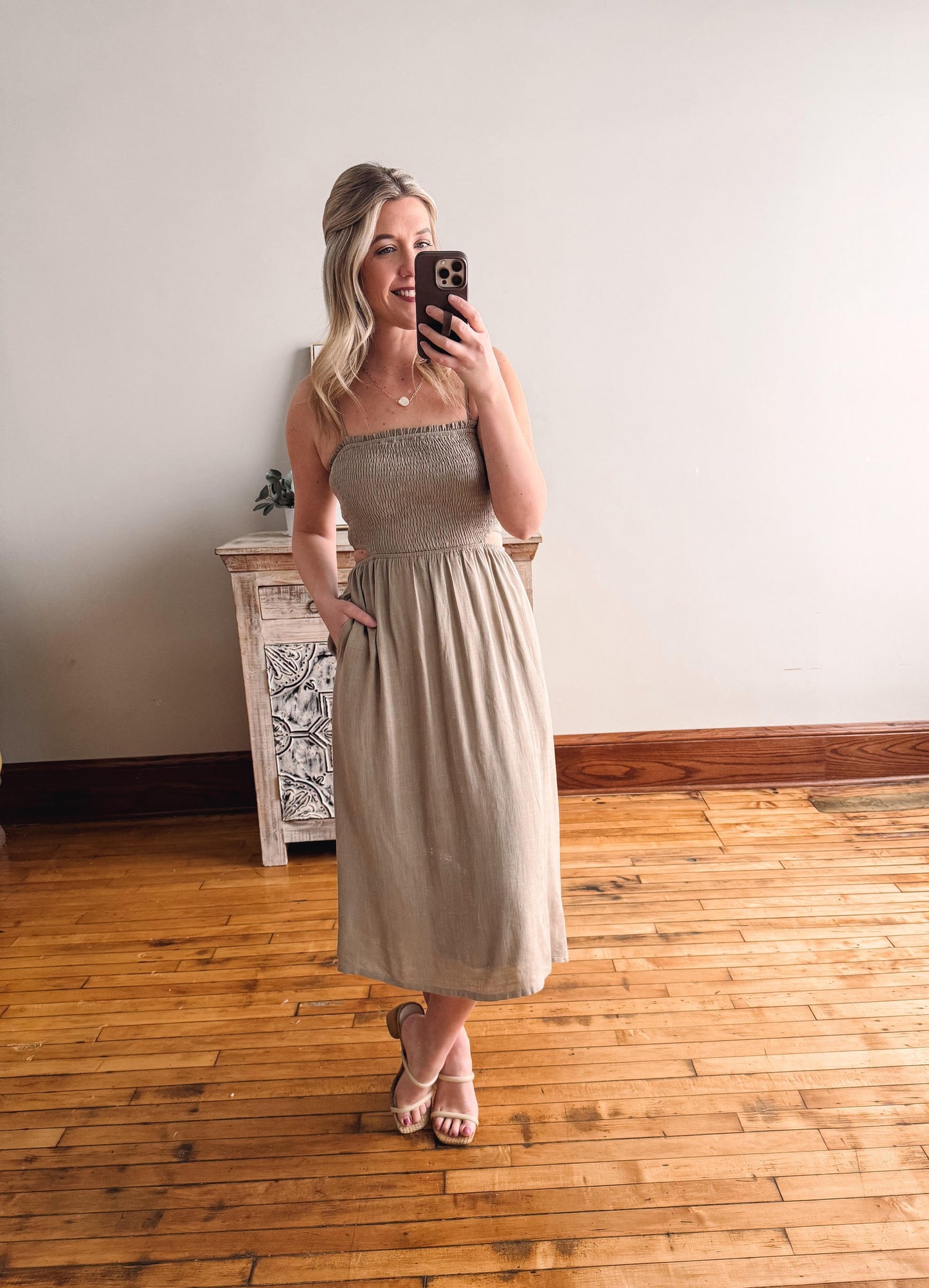 Woman taking a mirror selfie wearing a beige dress in a room with wooden flooring.