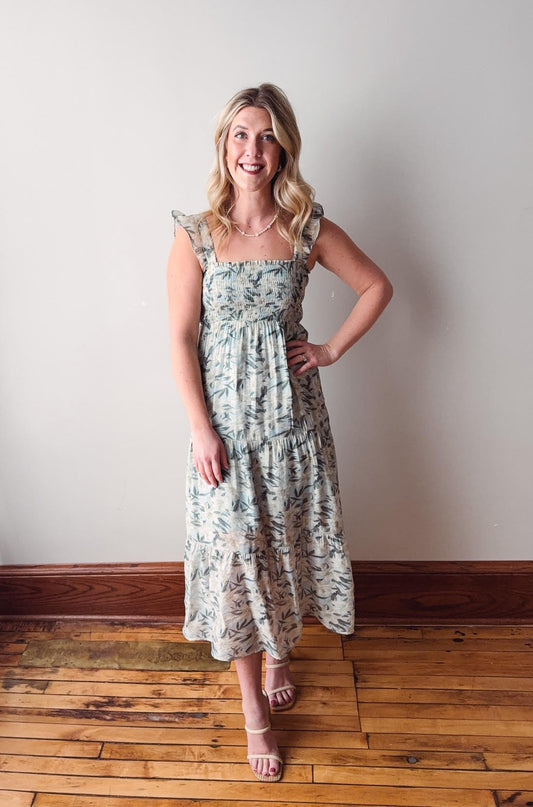 Woman wearing a floral dress standing on a wooden floor with a white wall background