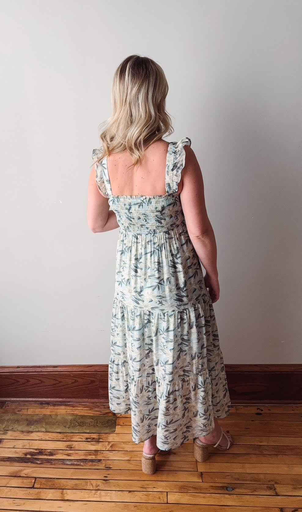 Woman wearing a floral dress standing on a wooden floor with a white wall background