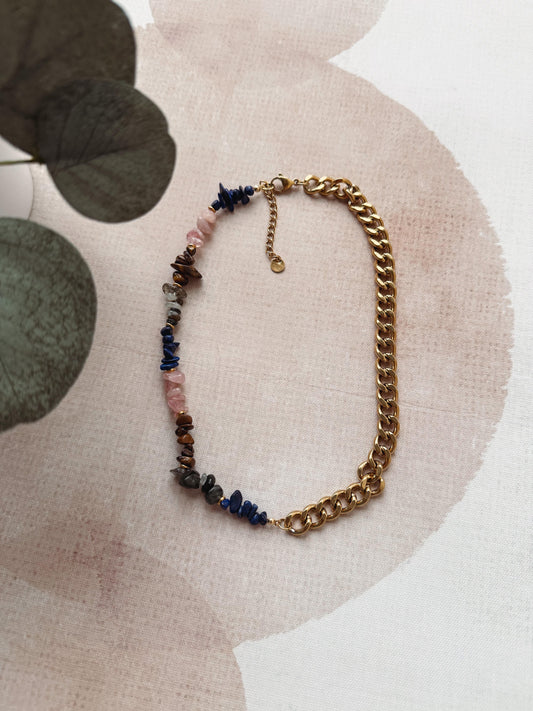Necklace with gold chain and multicolored beads on a textured surface with leaves.