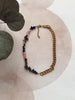 Necklace with gold chain and multicolored beads on a textured surface with leaves.