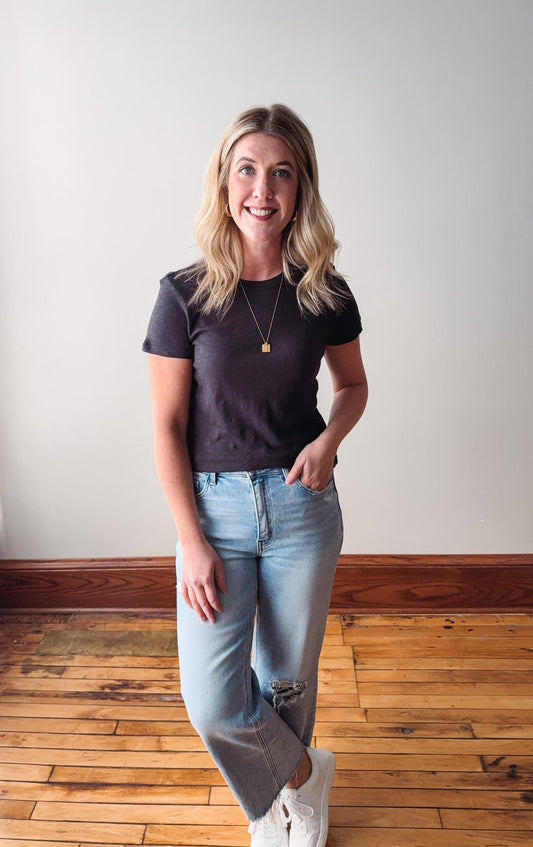 Woman wearing a black t-shirt and light blue jeans standing on a wooden floor.