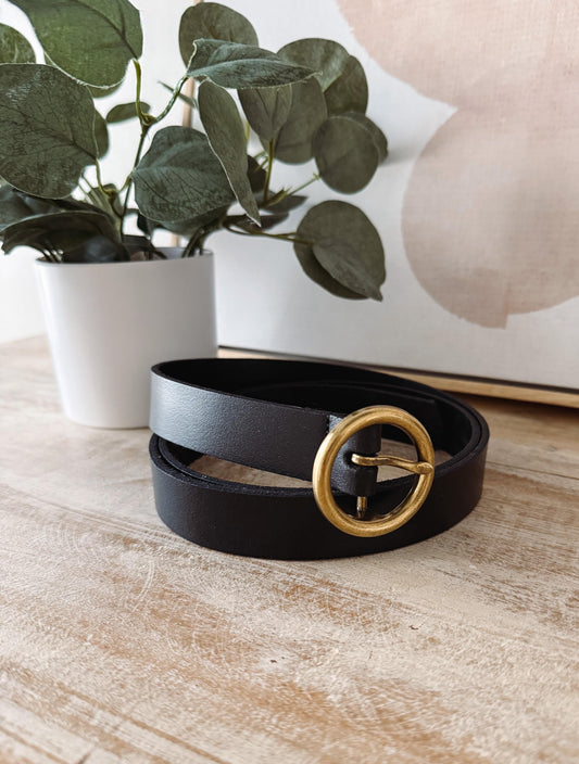 Black belt with a gold buckle on a wooden surface with a plant in the background
