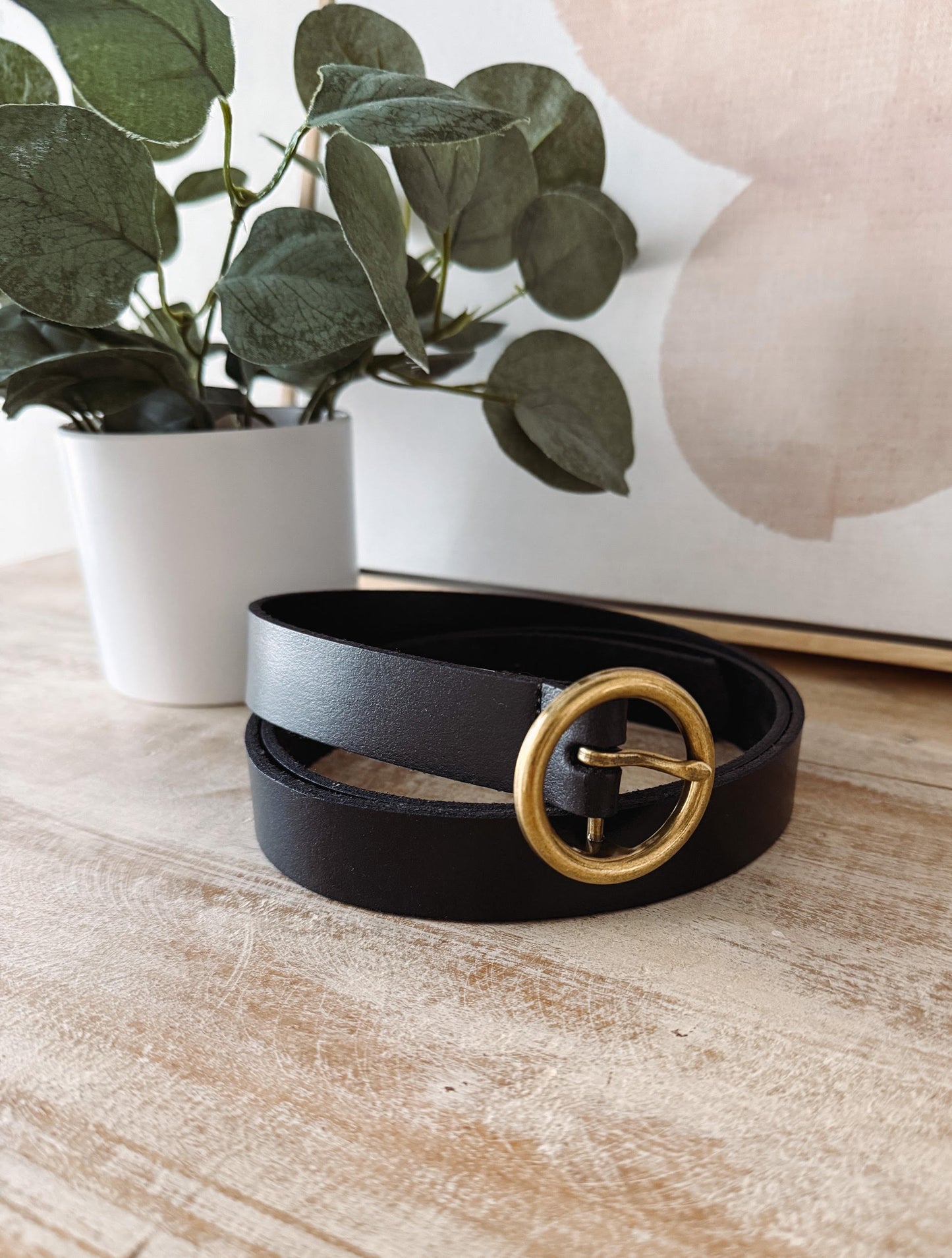 Black belt with a gold buckle on a wooden surface with a plant in the background