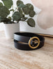 Black belt with a gold buckle on a wooden surface with a plant in the background