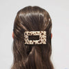 Person with leopard print hair clip in brown hair on a light gray background