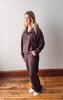 Woman wearing a brown tracksuit standing on a wooden floor with a white wall background