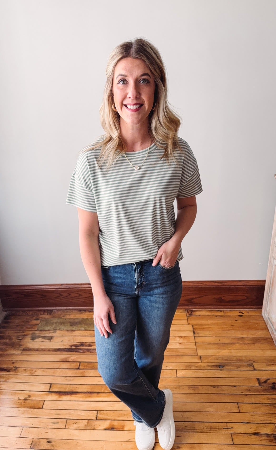 Woman wearing a striped shirt and jeans standing on a wooden floor.