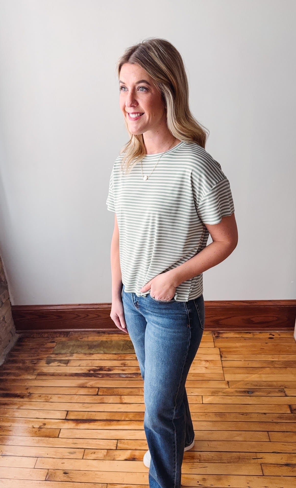 Woman wearing a striped shirt and jeans standing on a wooden floor.