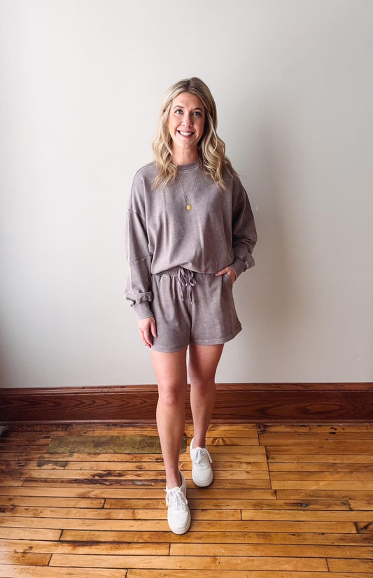Woman wearing a gray loungewear set standing on a wooden floor against a white wall.
