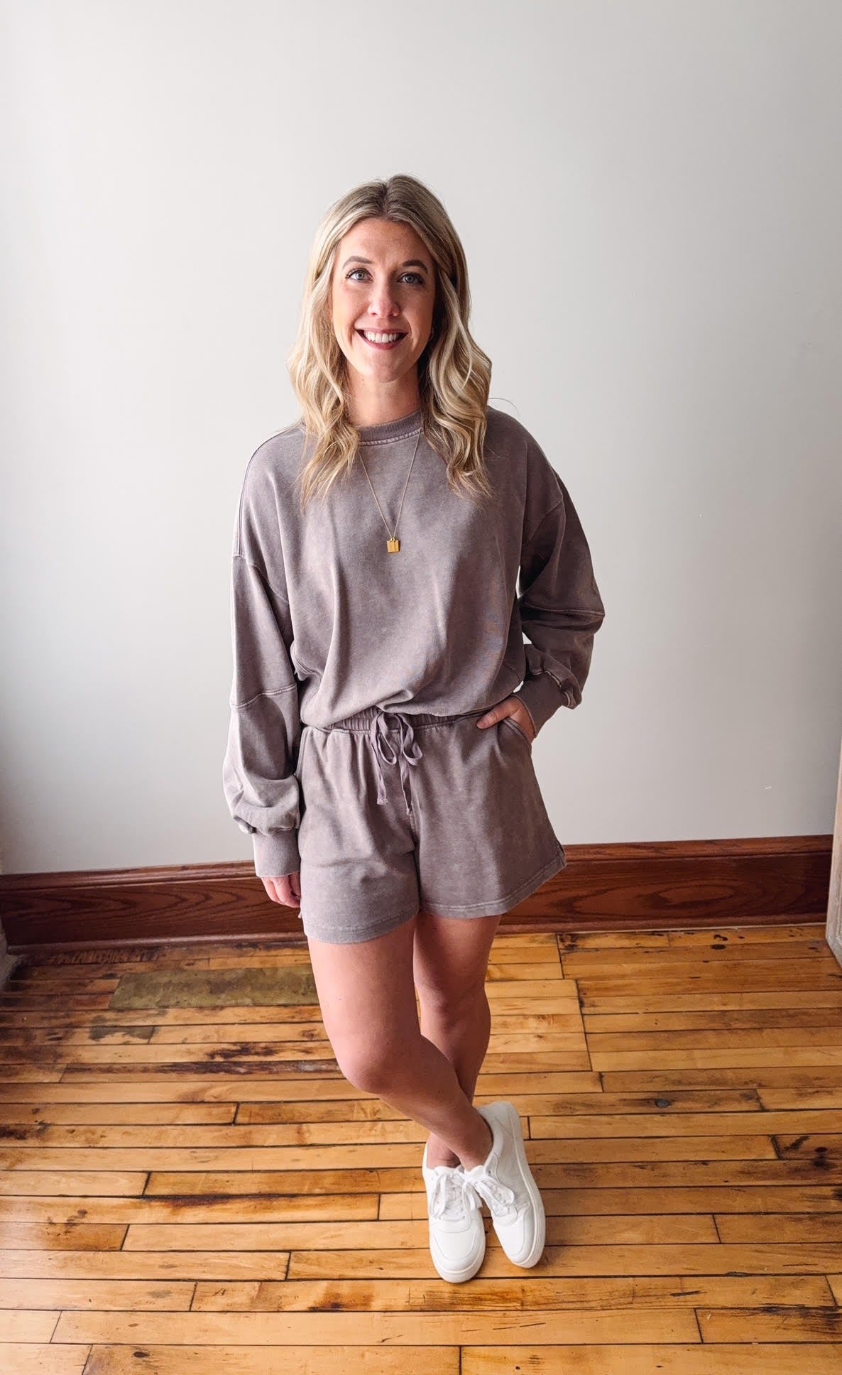 Woman wearing a gray sweatshirt and shorts set on a wooden floor.