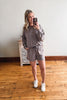 Woman taking a mirror selfie wearing a gray sweatshirt and shorts set on a wooden floor.