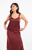 A woman modeling a satin slip dress in a deep burgundy color against a plain white studio background.