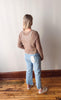 Person wearing a sheer brown top and blue jeans standing against a white wall.