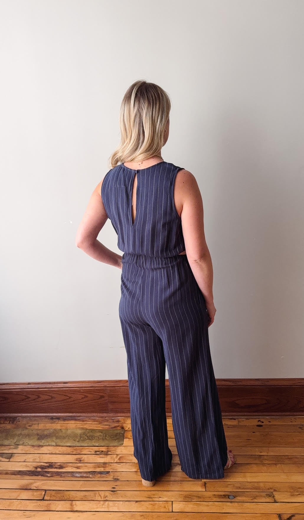 Woman wearing a navy striped jumpsuit standing against a white wall.