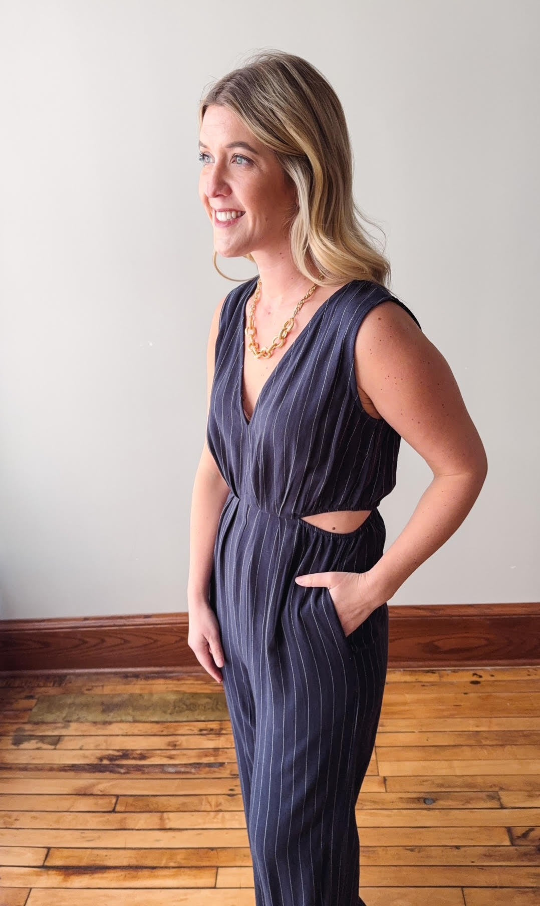 Woman wearing a dark blue jumpsuit with cut-out design, standing on a wooden floor.