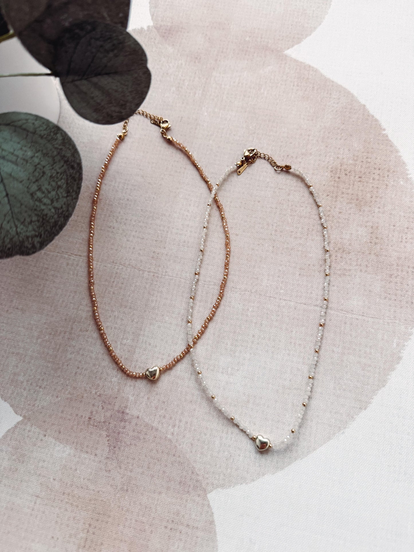 Two delicate necklaces on a textured surface with floral elements
