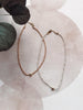 Two delicate necklaces on a textured surface with floral elements