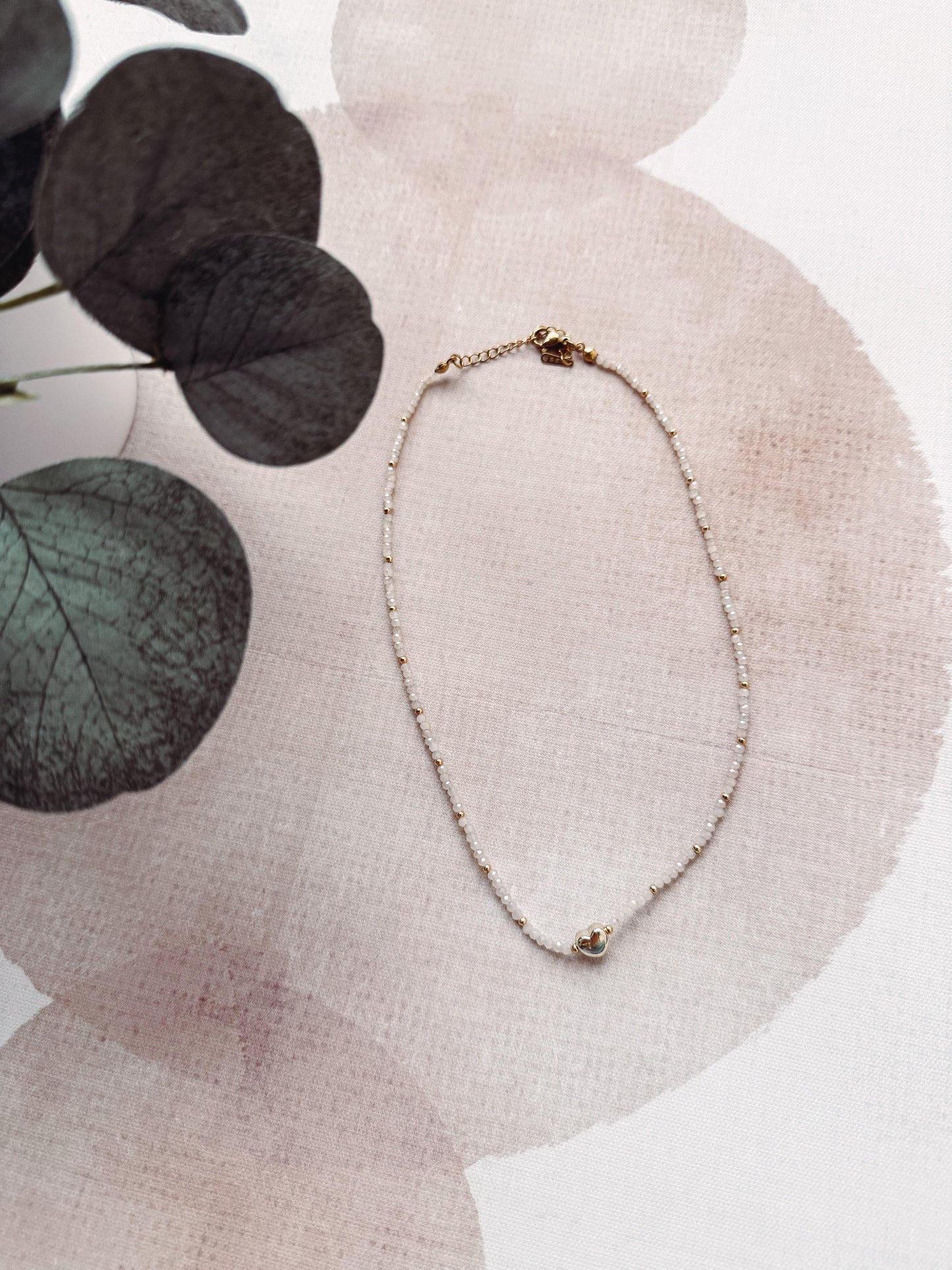 Delicate necklace on a textured surface with eucalyptus leaves