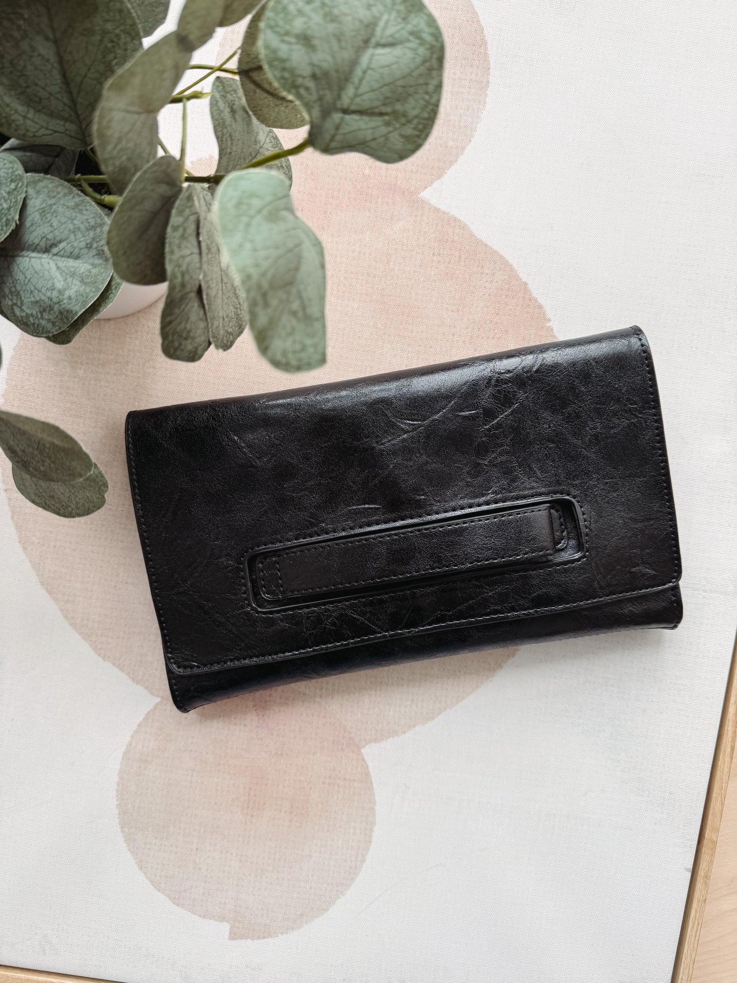 Black leather wallet on a light background with green leaves