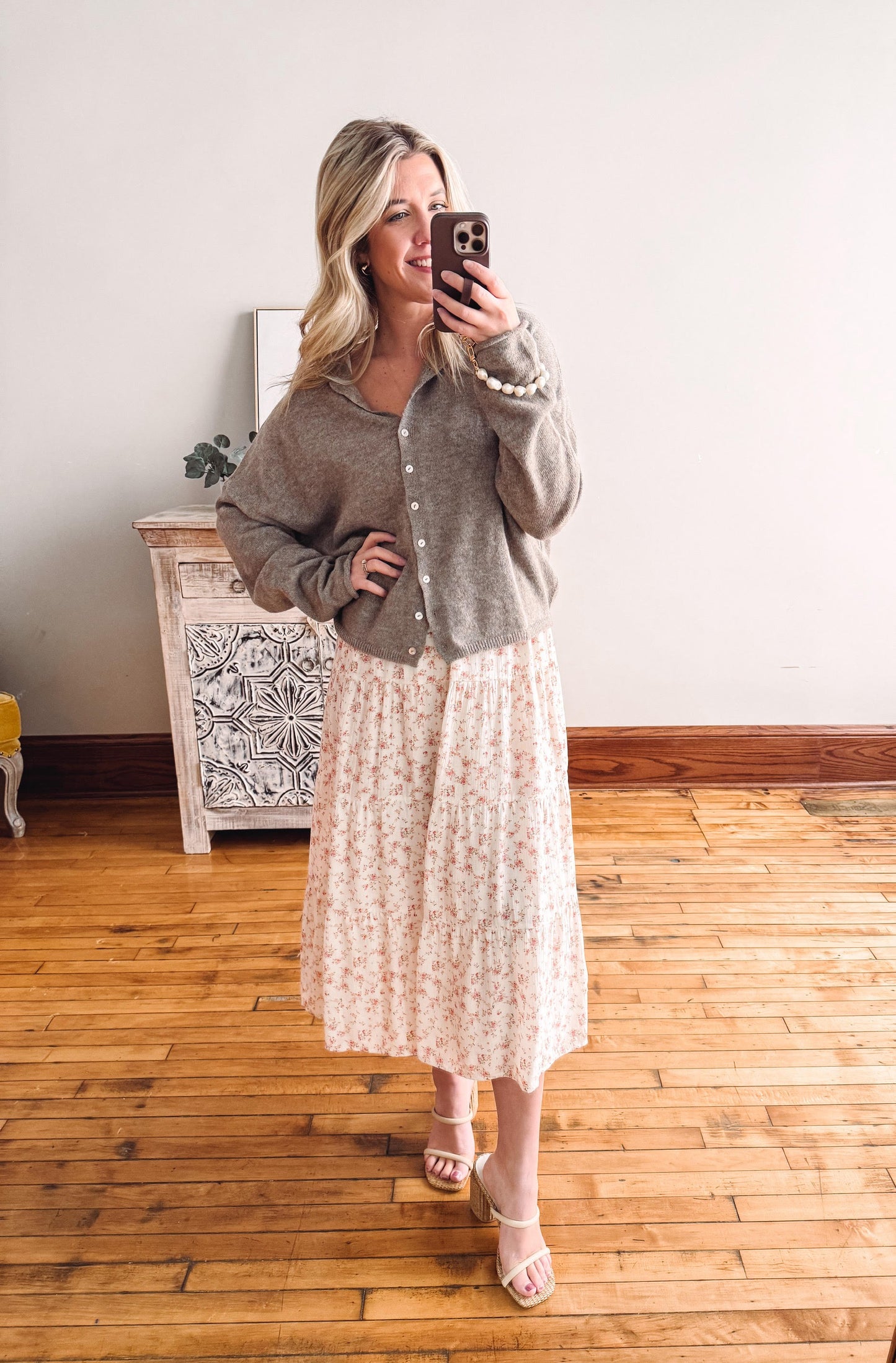Woman taking a mirror selfie wearing a gray shirt over a white dress with a floral pattern.