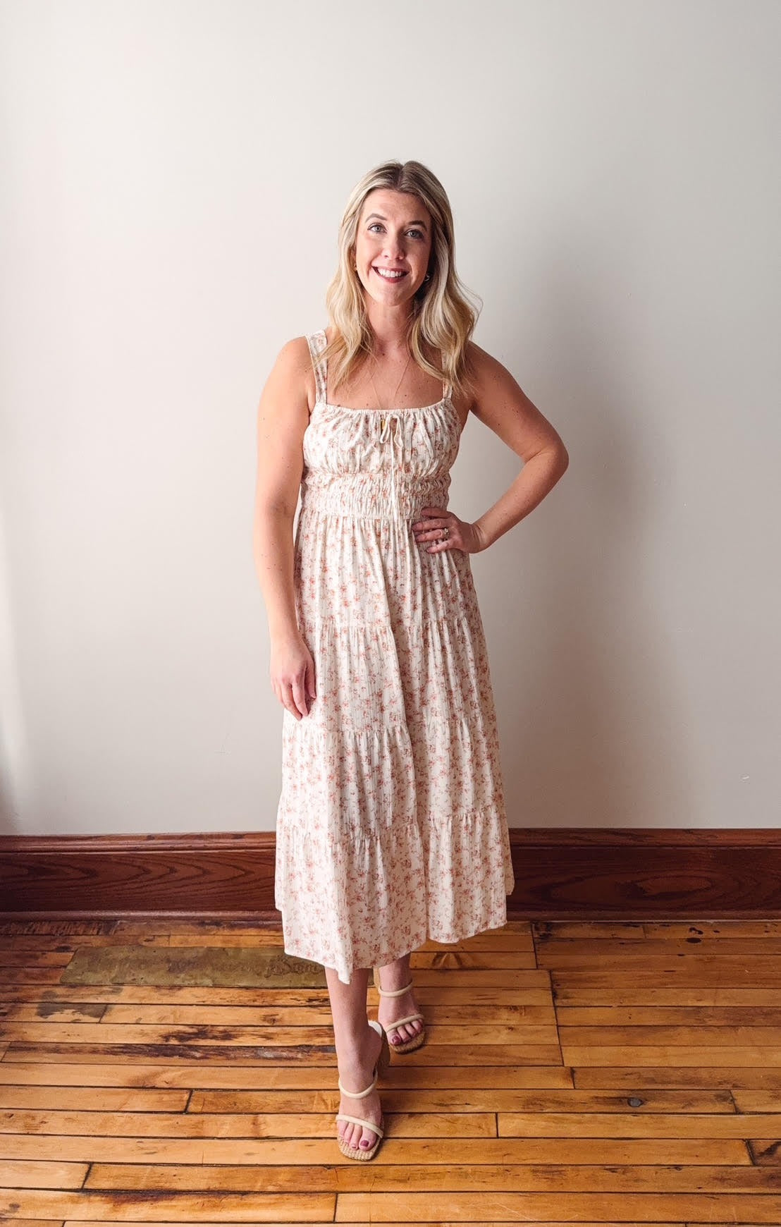 Woman in a floral dress standing on a wooden floor against a white wall