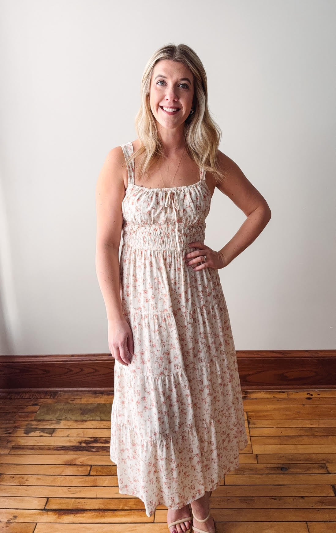 Woman wearing a floral dress standing on a wooden floor with a white wall background