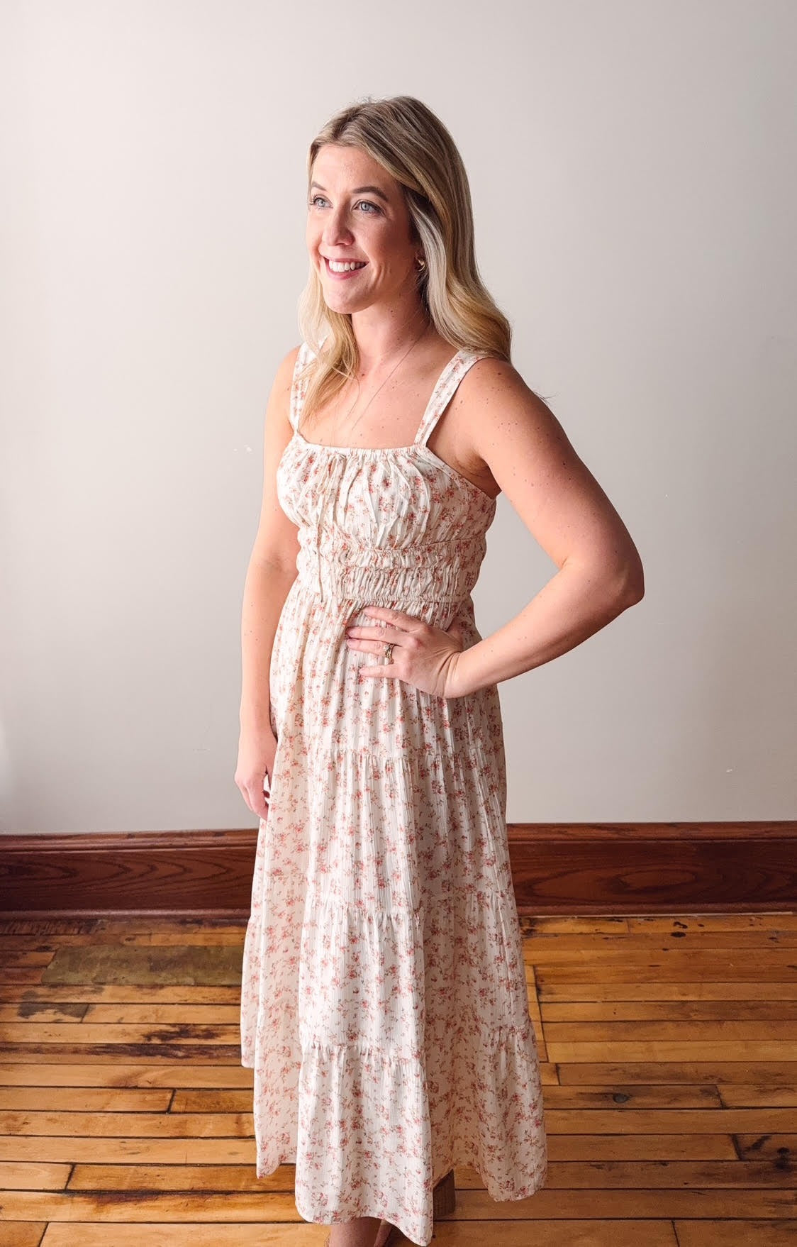Woman wearing a floral dress standing on a wooden floor with a white wall background