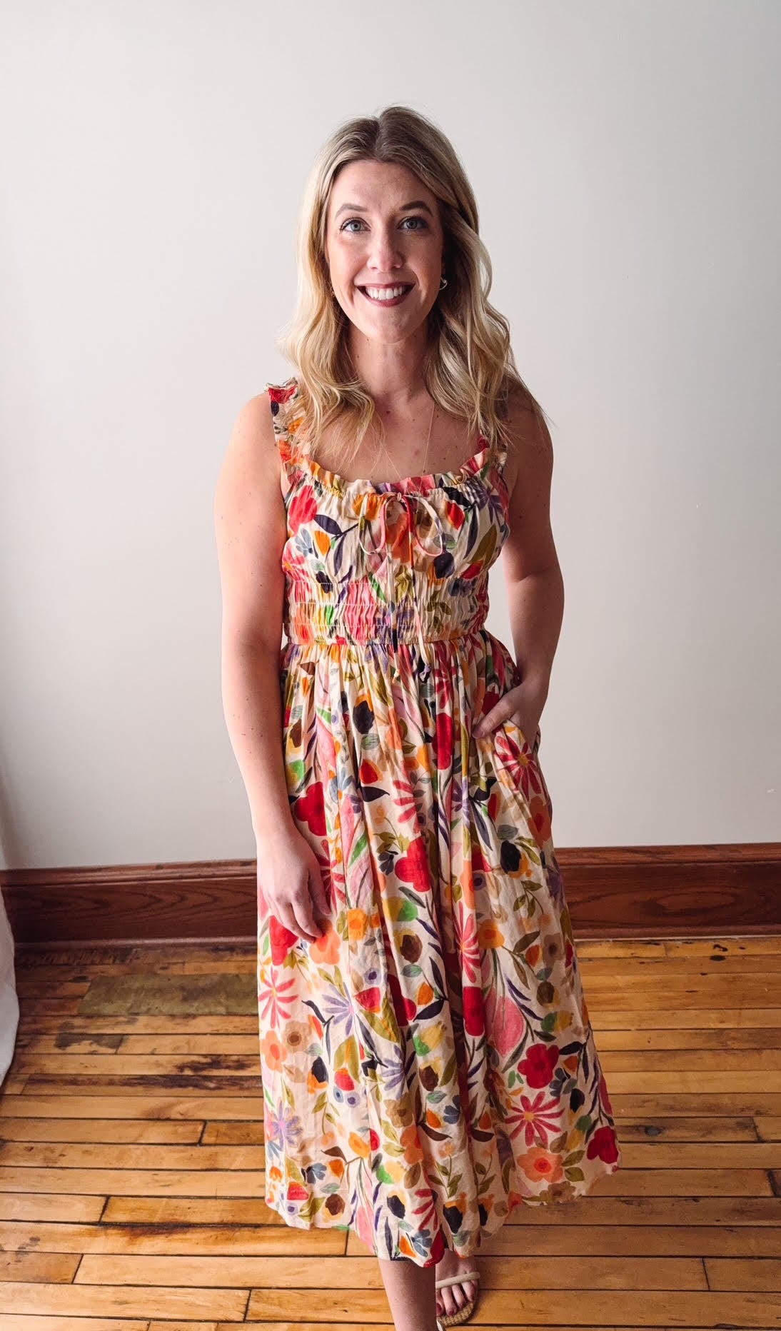 Woman wearing a colorful floral dress standing on a wooden floor.