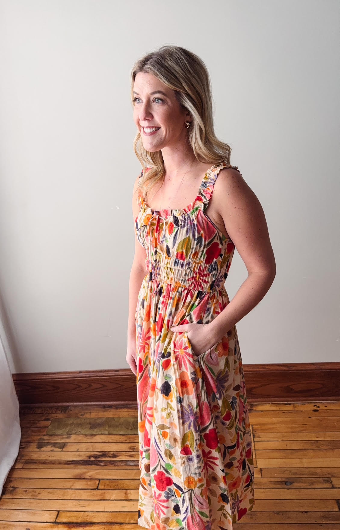 Woman wearing a colorful floral dress standing in a room with wooden flooring.