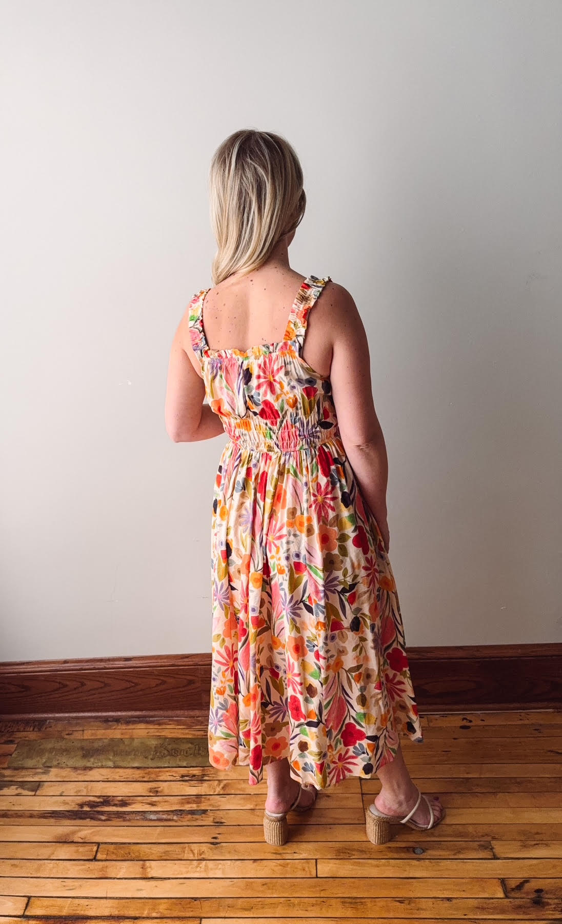 Woman wearing a colorful floral dress standing on a wooden floor with a white wall background