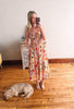 Woman in a floral dress taking a mirror selfie with a dog on a wooden floor.