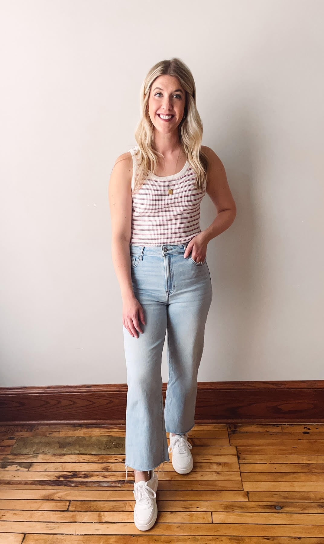 Woman in striped tank top and light jeans standing against a plain background