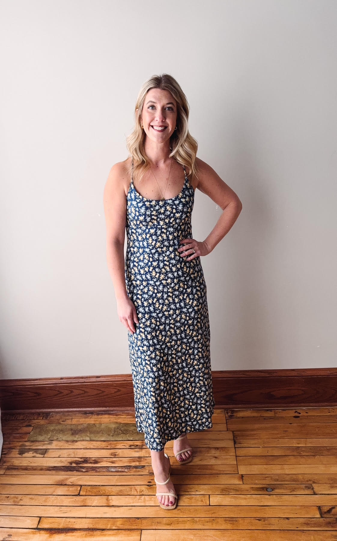 Woman wearing a floral dress standing on a wooden floor against a white wall.