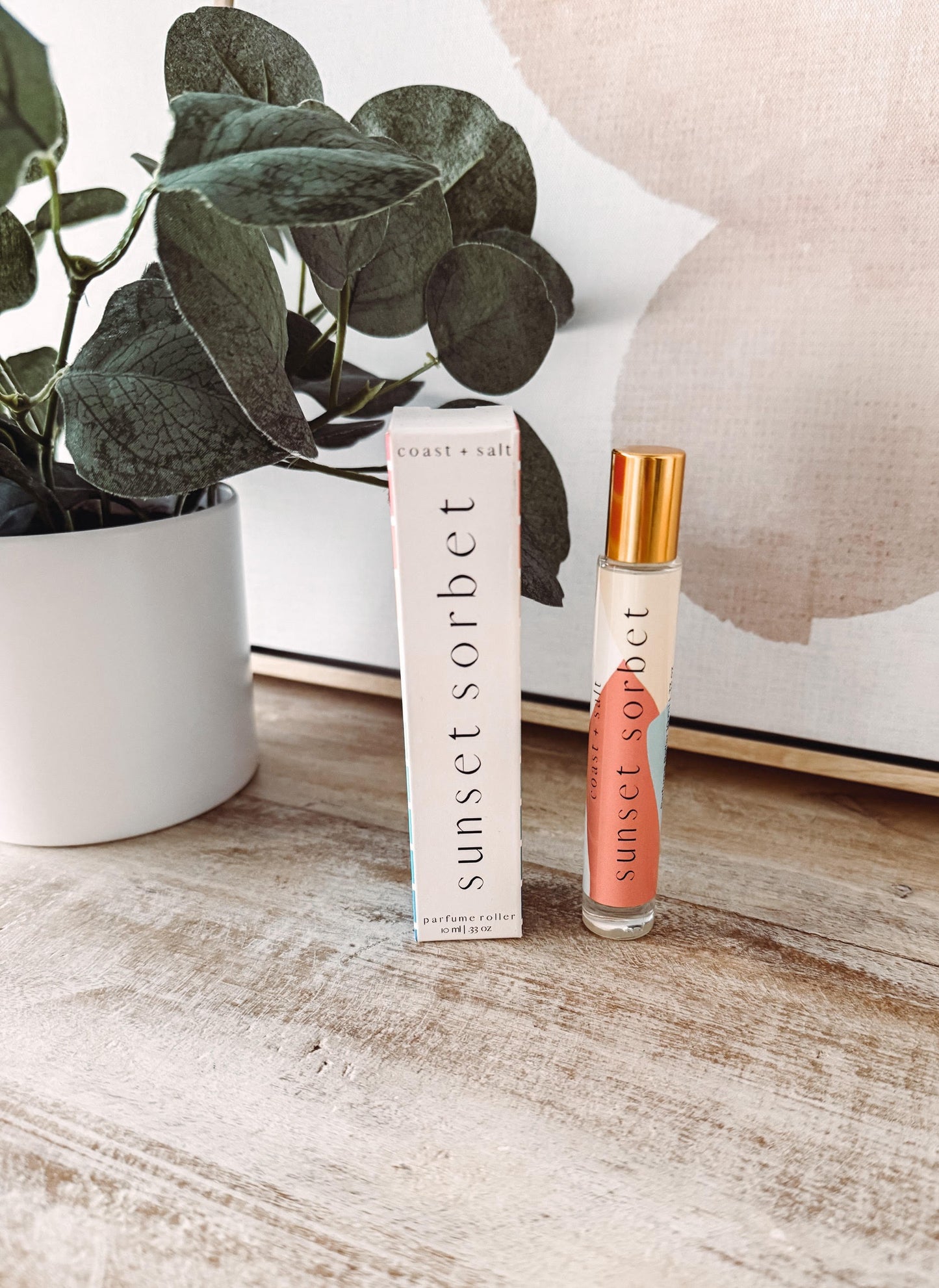 Sunset Sorbet perfume bottle and packaging on a wooden surface with a plant in the background