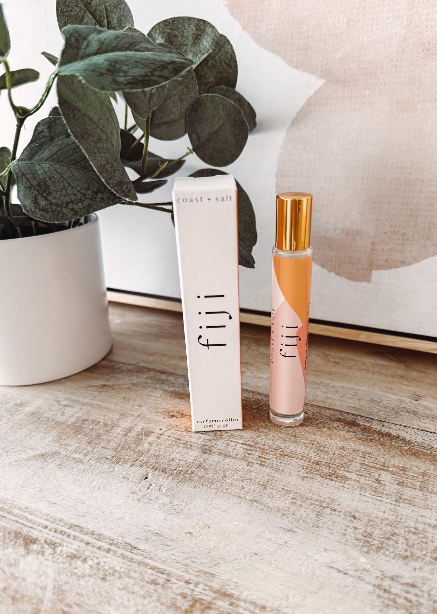 Fiji perfume bottle and packaging on a wooden surface with a plant in the background