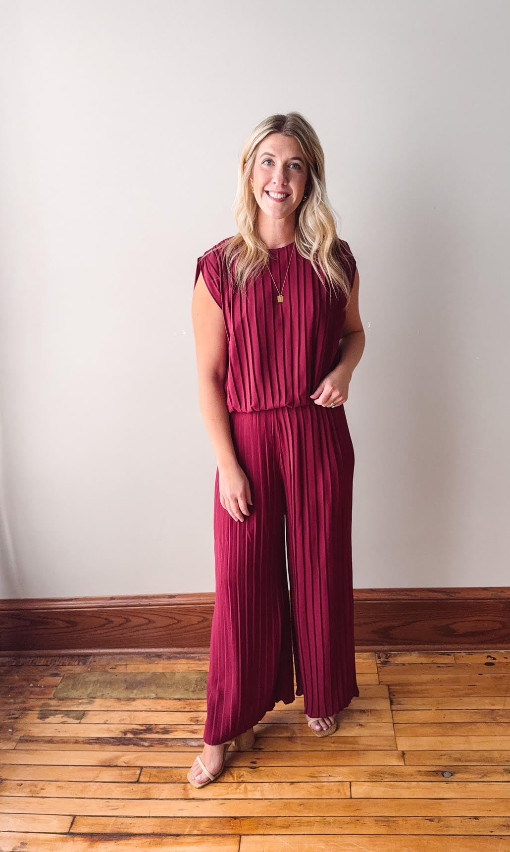 Woman wearing a burgundy jumpsuit standing against a plain white wall.