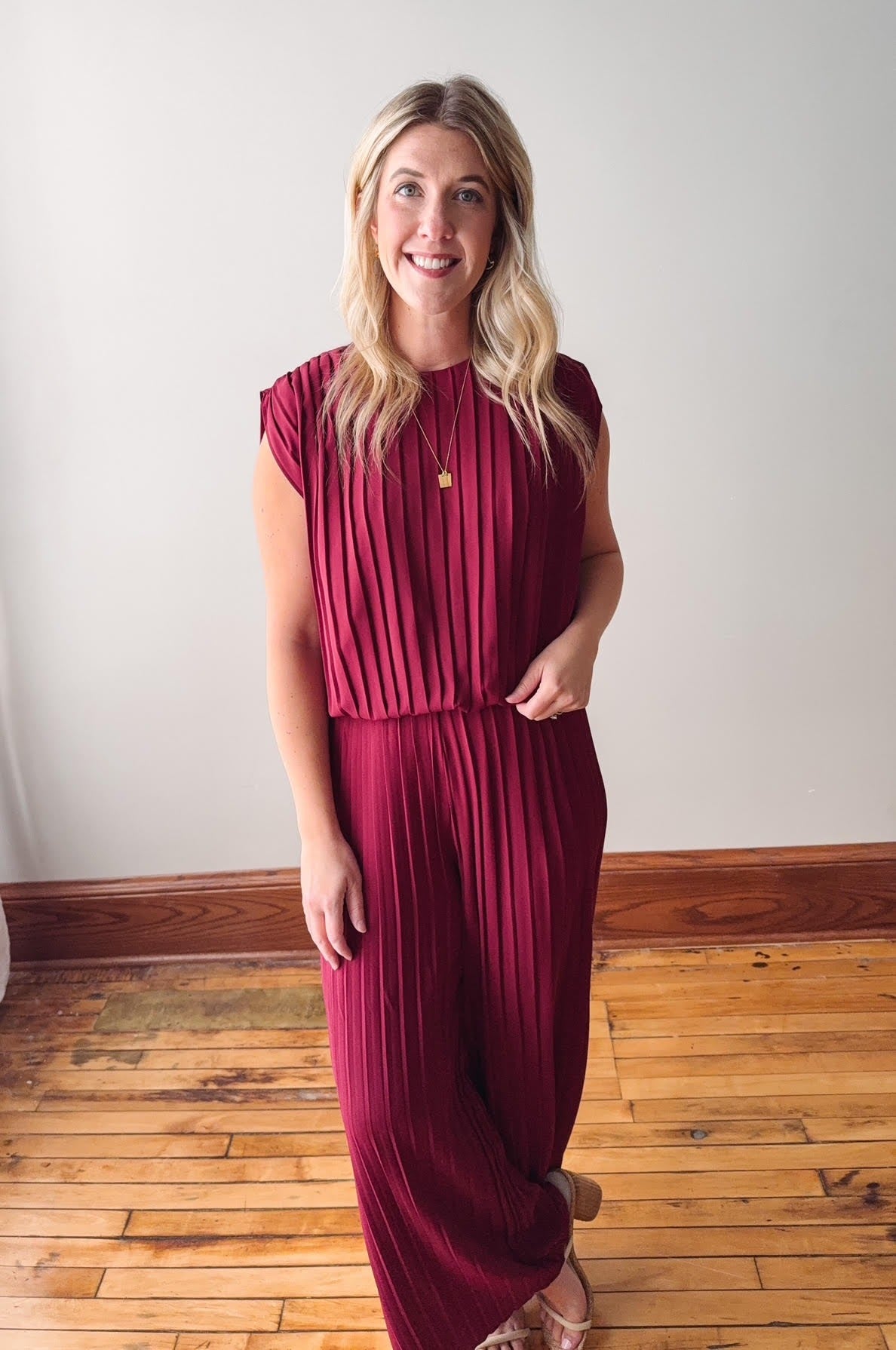 Woman wearing a burgundy pleated dress standing on a wooden floor.