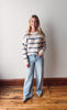 Woman wearing a striped sweater and jeans standing against a plain wall.