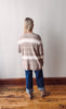 Person wearing a striped sweater and jeans standing on a wooden floor against a white wall.