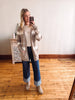 Woman taking a mirror selfie wearing a long plaid cardigan, white shirt, blue jeans, and beige boots.