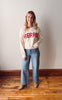 Woman wearing a sweater with 'MERRY' text standing on a wooden floor.
